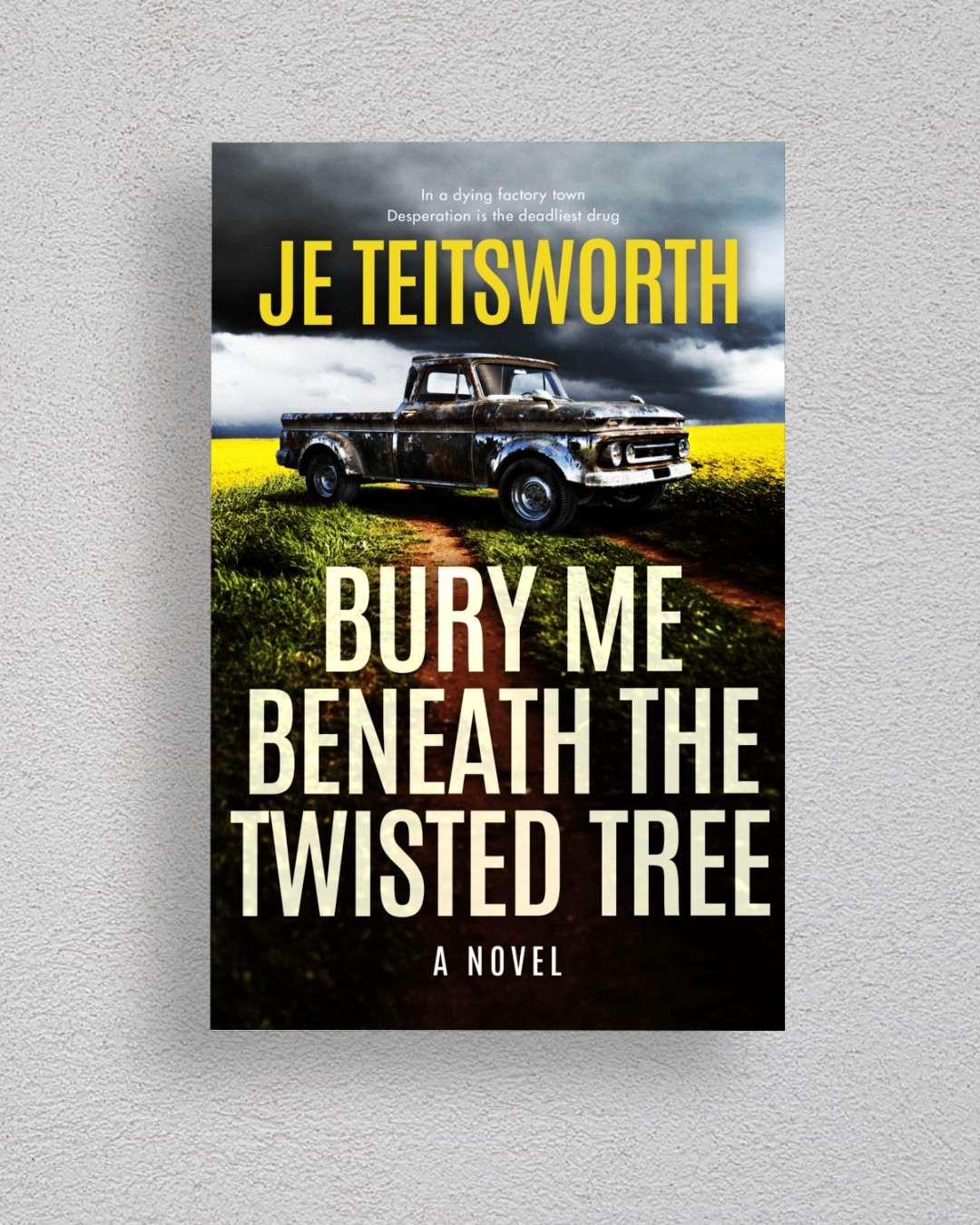 A book cover for the novel 'Bury Me Beneath the Twisted Tree' by Je Teisworth, displayed against a light gray textured wall. The cover features a dramatic scene of an old pickup truck parked on a dirt path in a field of yellow flowers under a stormy sky.